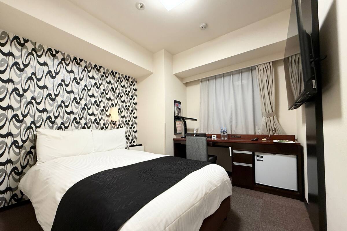 A hotel room with a bed, a desk, a television, and a window with curtains.