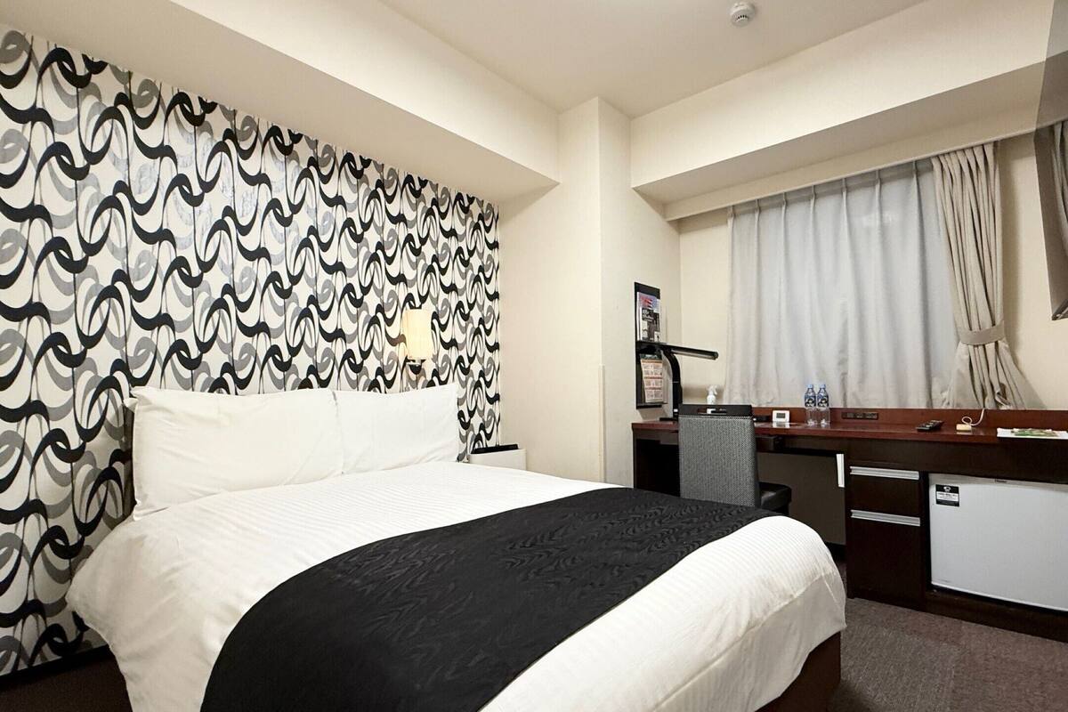 A hotel room with a bed, a desk, a chair, a TV, and a window with curtains.