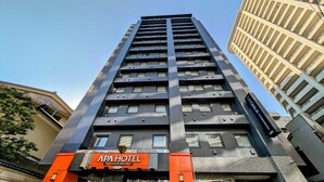 Un moderno edificio de hotel con una fachada destacada en naranja y negro, que presenta una entrada amplia con puertas de vidrio y un letrero que dice "APA HOTEL".