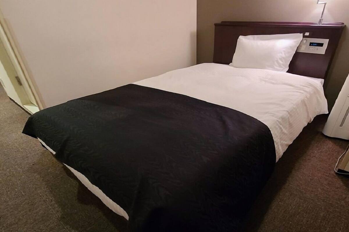 A hotel room with a bed, a bedside table, and a wall-mounted control panel.