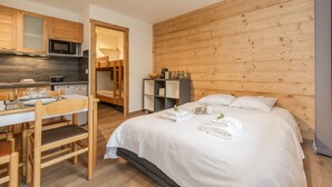 A hotel room with a wooden headboard, a bed with white linens, a dining area with a table and chairs, and a kitchenette with a microwave. - Cham Sud Grepon102 Mountain-View Balcony for 4, Chamonix, France (Chamonix)