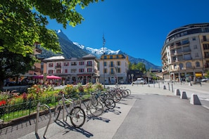 Rua com bicicletas estacionadas ao longo da calçada, edifícios com varandas e uma montanha ao fundo.