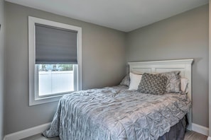 A bedroom with a bed, a window with blinds, and a white headboard. - Narragansett Escape by Narrow River & Beaches (Narragansett)