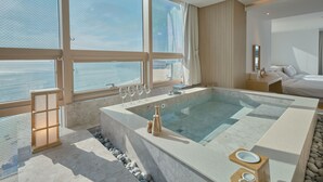 Une salle de bain moderne avec une grande baignoire, un banc en bois et une vue sur la mer grâce à de grandes fenêtres.