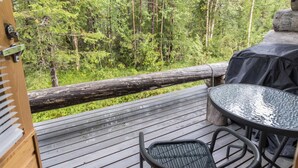En träaltan med ett glasbord och stolar, med utsikt över ett skogsområde.
