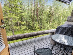 Eine Holzterrasse mit einem Metalltisch und -stühlen, mit Blick auf ein bewaldetes Gebiet.