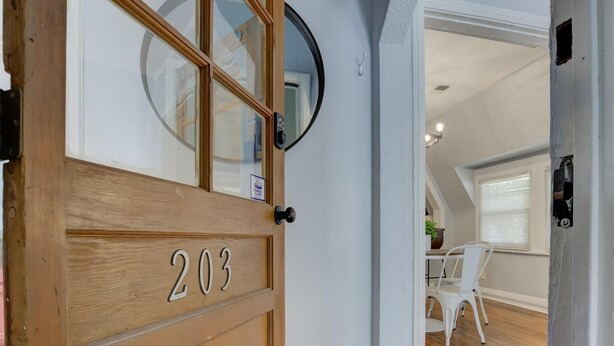 A wooden door with the number 203, a round mirror, and a view into a room with a white chair and a table.