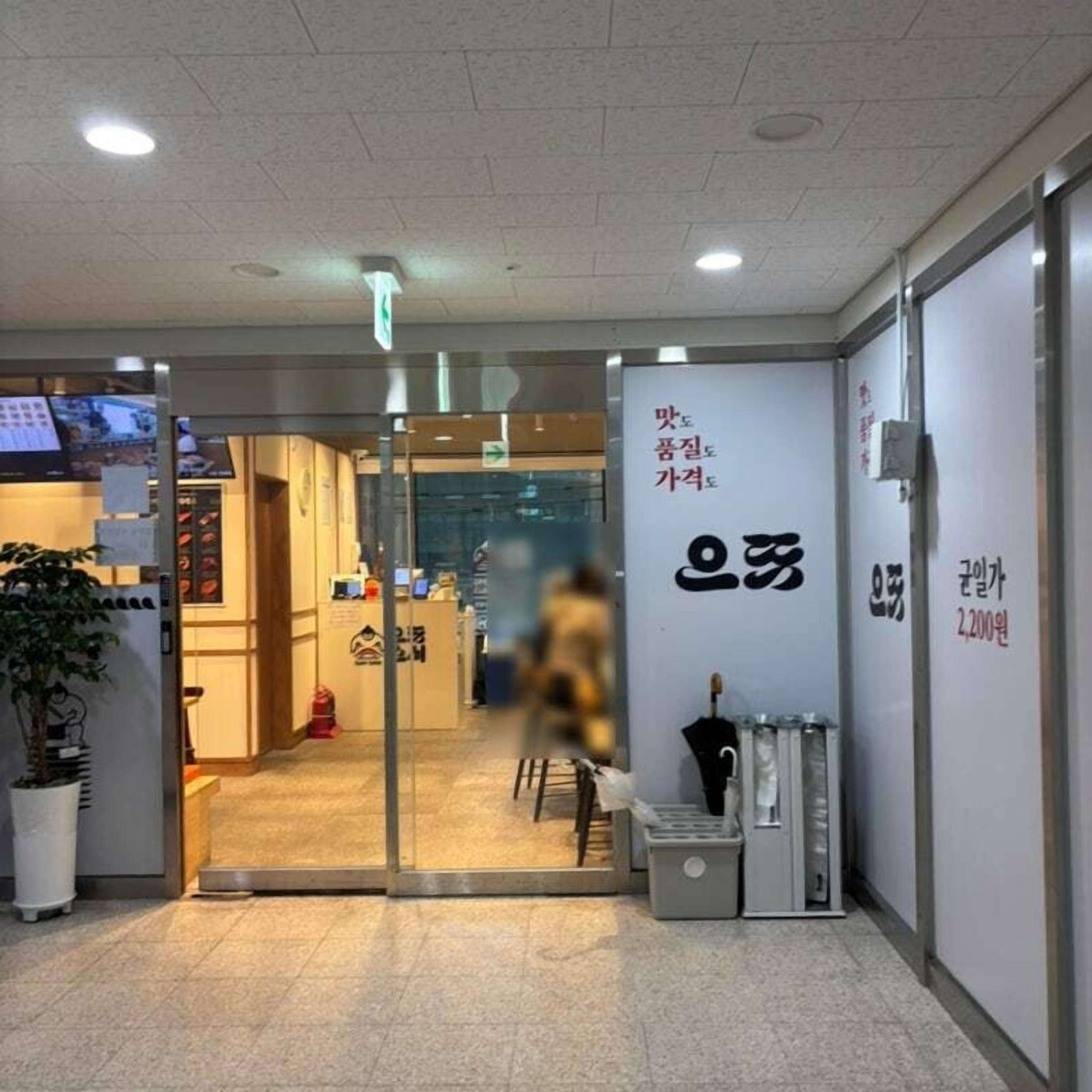 A hotel entrance with a reception desk, a glass door, and a sign with Korean text.