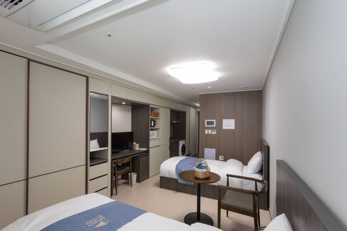 A hotel room with a bed, a desk, a chair, a small table, and a television.