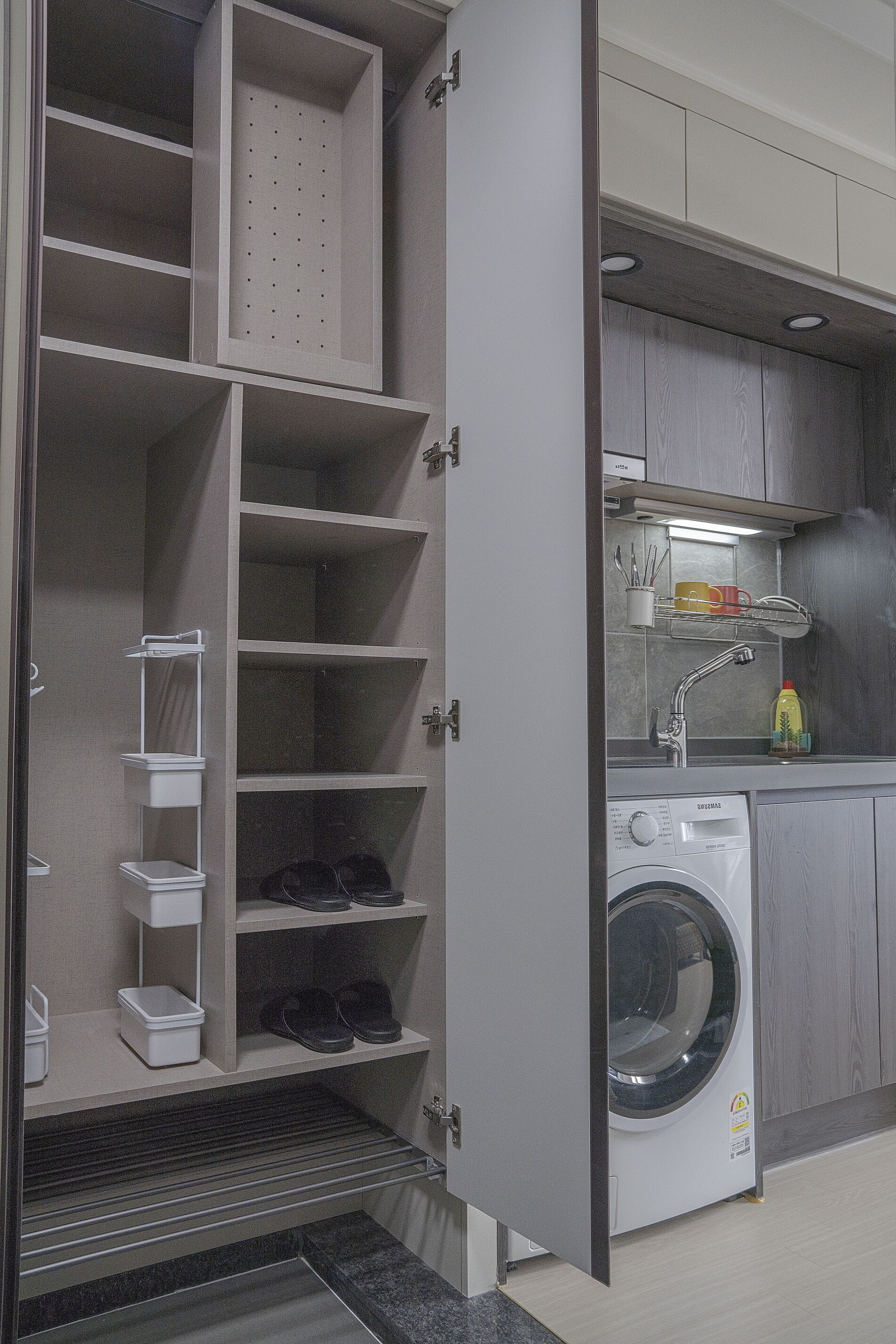 A laundry room with a washing machine, shelves for storage, and a sink with a mirror.