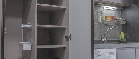 A laundry room with a washing machine, shelves for storage, and a sink with a mirror.