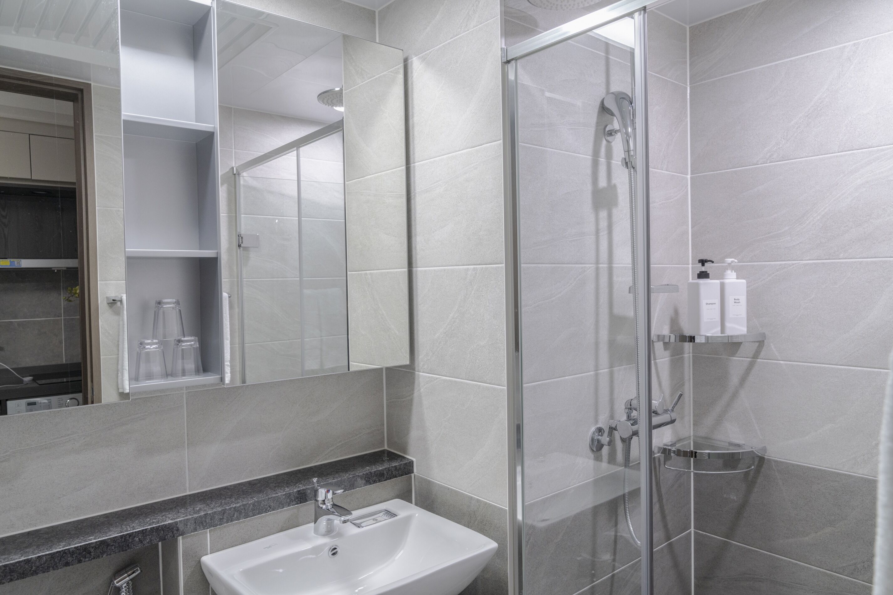 Un baño moderno con ducha envuelta en vidrio, un lavamanos y un espejo.