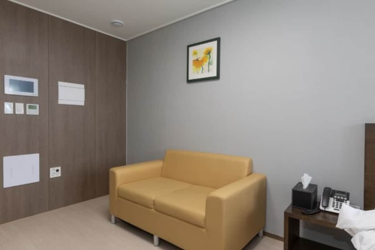 A modern room with a beige sofa, a small wooden table with a phone and tissues, and a framed picture on the wall.