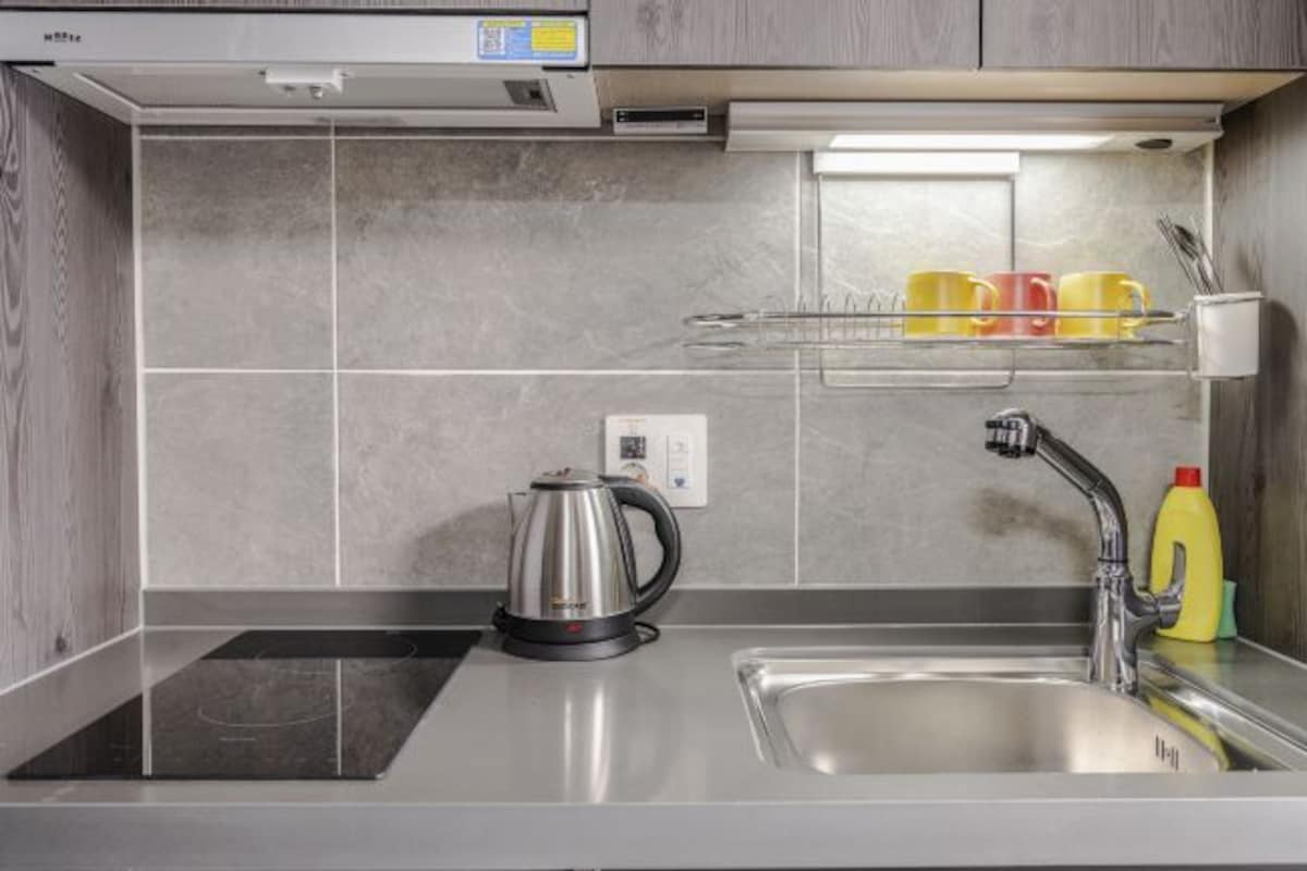 A modern kitchen with a stainless steel sink, a kettle, and a dish drying rack.