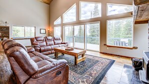 A spacious living room with leather sofas, a coffee table, and large windows offering a view of the outdoors. - Hot Tub & Forest Views - 3,650 Sq Ft, Two Living Rooms, Pet-Friendly, 26mi Breck (Fairplay)