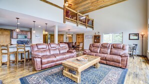 A spacious living room with two leather sofas, a coffee table, and a patterned rug. A wooden ceiling and staircase are visible in the background. - Hot Tub & Forest Views - 3,650 Sq Ft, Two Living Rooms, Pet-Friendly, 26mi Breck (Fairplay)