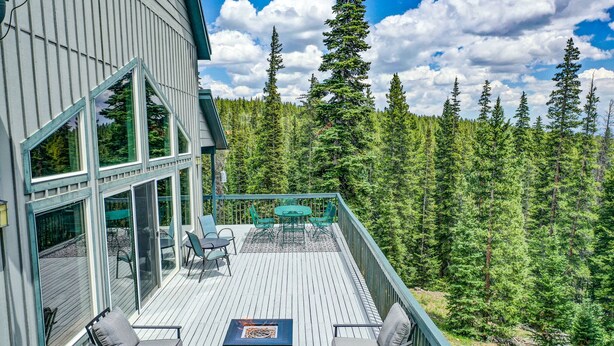 A wooden deck with outdoor furniture and a fire pit, surrounded by a forested landscape. - Hot Tub & Forest Views - 3,650 Sq Ft, Two Living Rooms, Pet-Friendly, 26mi Breck (Fairplay)