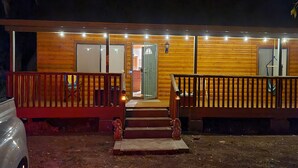 Een houten chalet met een veranda, trappen naar de ingang en een voertuig ervoor geparkeerd.