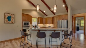 Une cuisine moderne avec des meubles en bois, des appareils en acier inoxydable, un îlot central doté de tabourets de bar et un éclairage suspendu.
