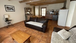 A living room with a wooden coffee table, a leather sofa, and a patterned armchair. A dining area with a table and chairs is visible in the background.
