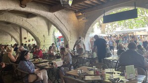 An outdoor café with stone arches, wooden tables, and chairs.
