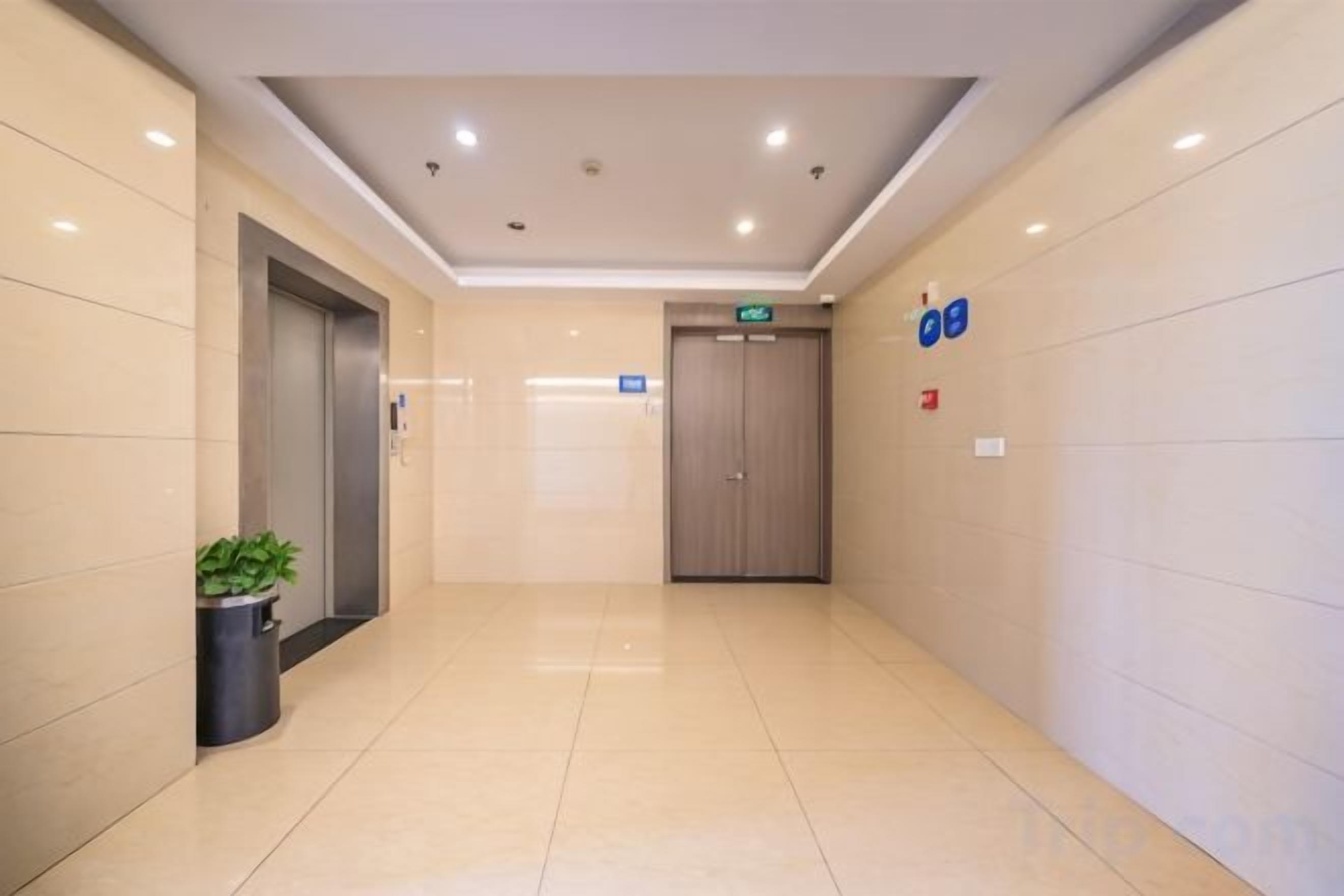 A hotel corridor with a door, an elevator, and a trash bin.