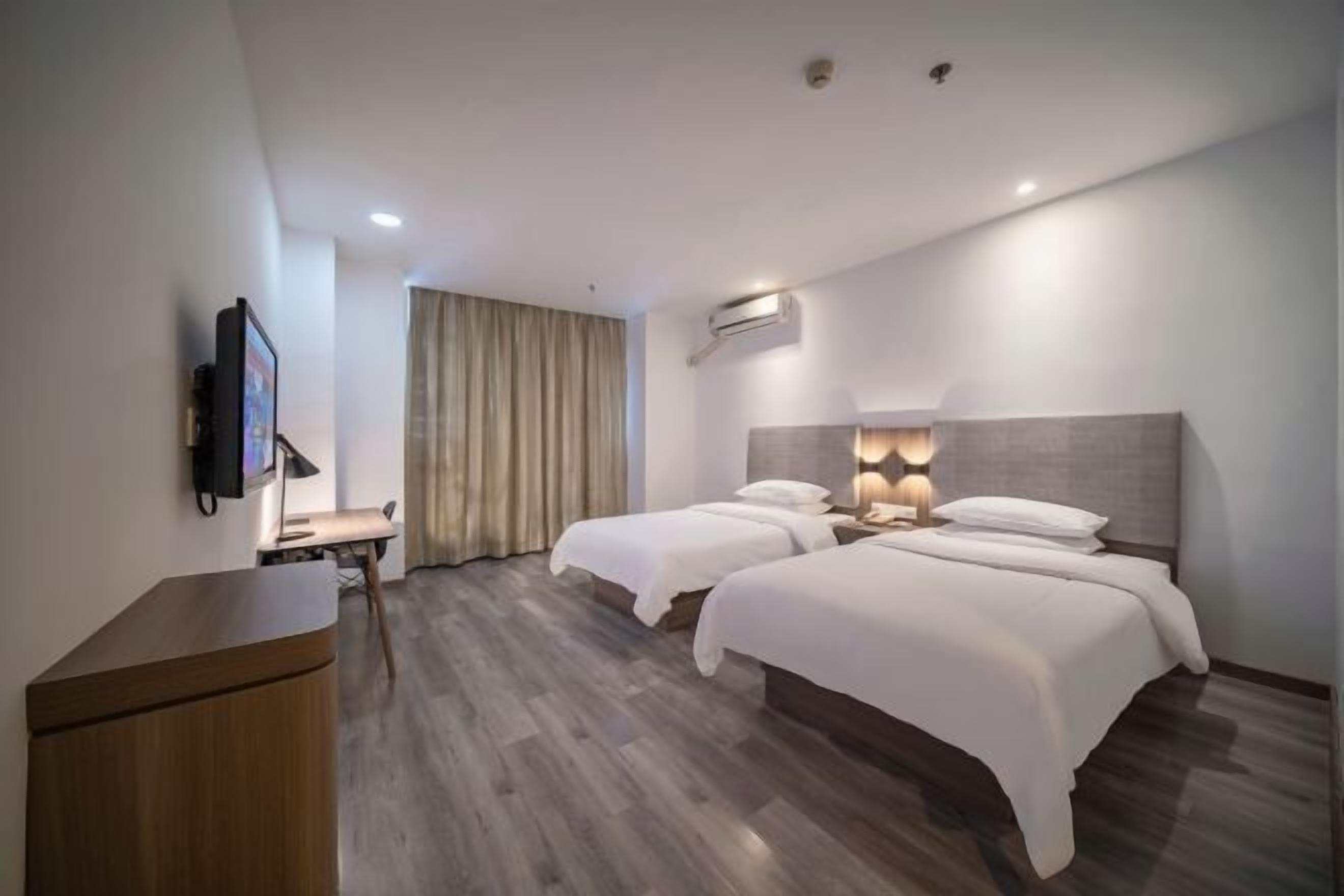 Quarto de hotel com duas camas, uma escrivaninha, uma televisão e um ar condicionado.