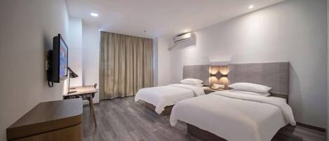 A hotel room with two beds, a desk, a TV, and an air conditioning unit.