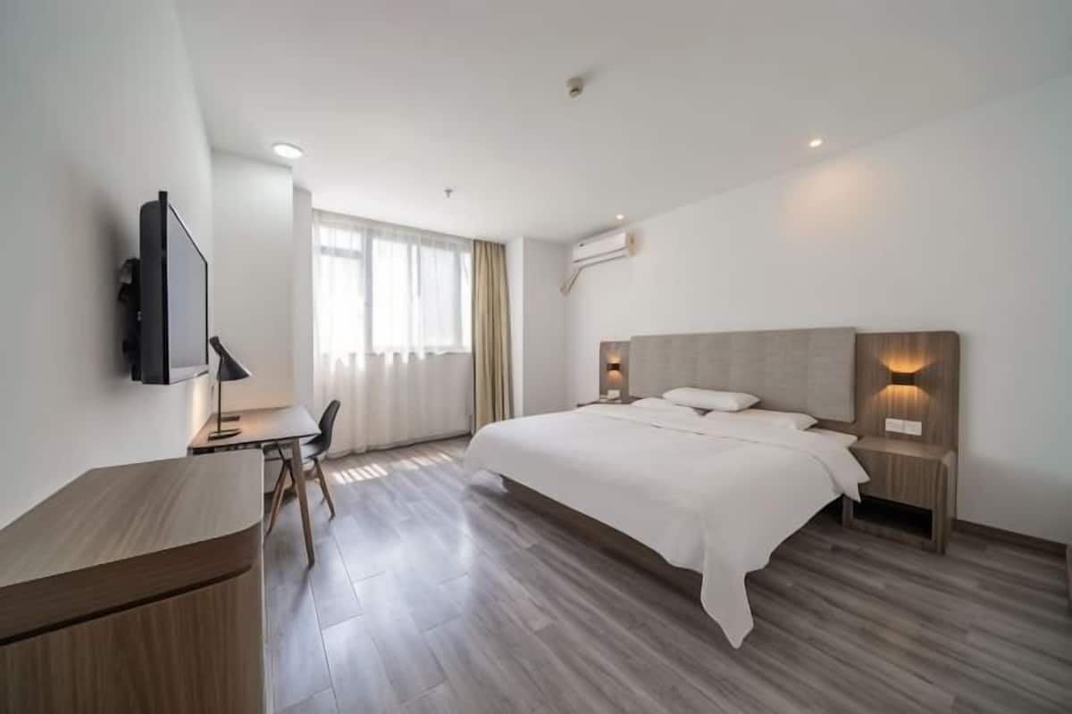 A modern hotel room with a large bed, a desk, a chair, a television, and a window with curtains.