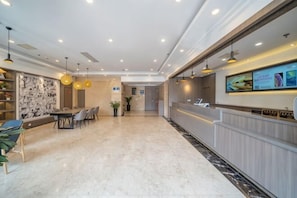 A hotel lobby with a reception desk, seating area, and a large wall with artwork. - Geli Hotel (Shanghai Kangqiao Subway Station store, New International Expo Center ) (Shanghai)