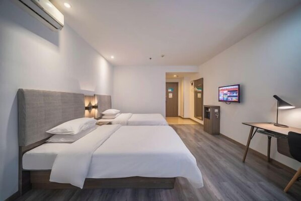 A hotel room with two beds, a desk, a TV, and an air conditioning unit.