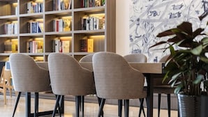 Uma biblioteca moderna com estantes, uma área de refeições com cadeiras e um vaso de planta.