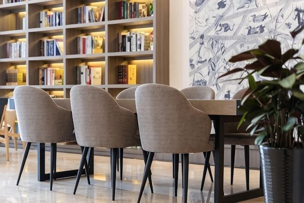 A modern library with bookshelves, a dining area with chairs, and a potted plant. - Geli Hotel (Shanghai Kangqiao Subway Station store, New International Expo Center ) (Shanghai)