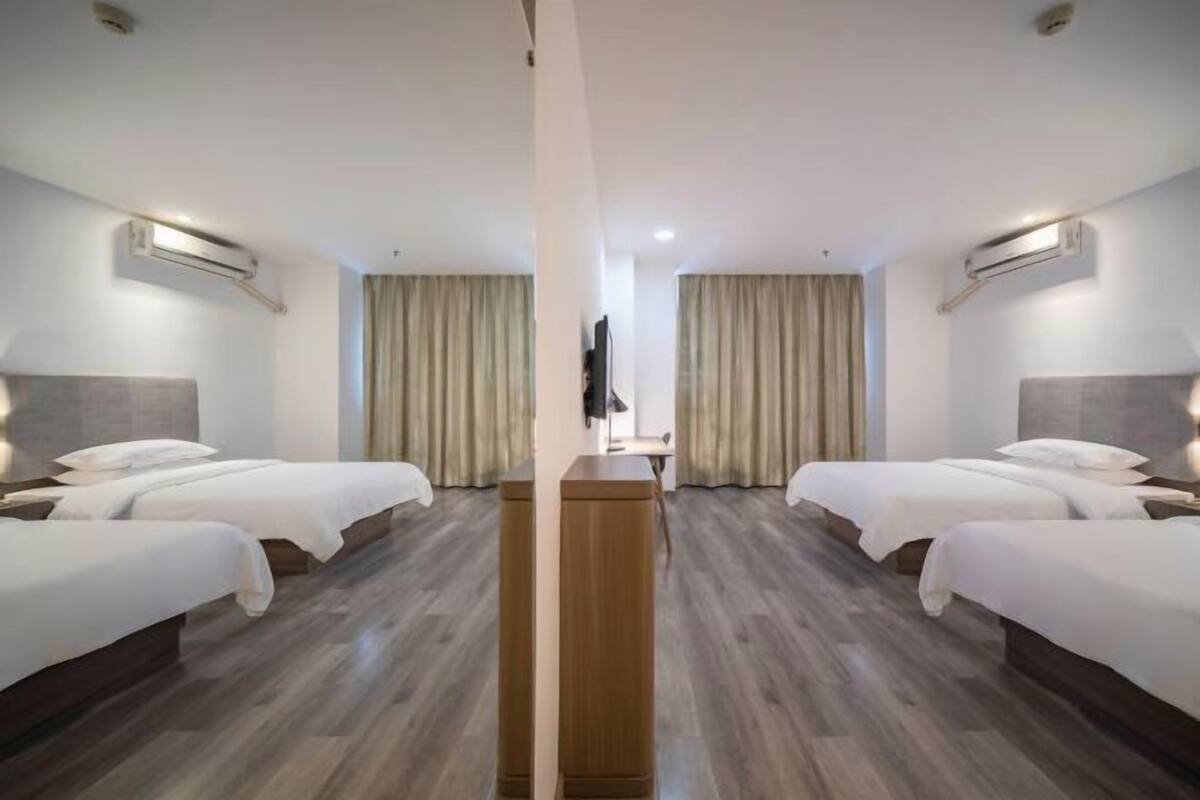 A hotel room with two beds, a wooden nightstand, a flat-screen TV, and a large window with curtains.