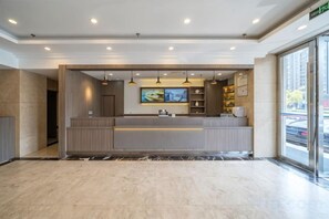 A modern hotel lobby with a reception desk, pendant lighting, and a large window offering a view of the street. - Geli Hotel (Shanghai Kangqiao Subway Station store, New International Expo Center ) (Shanghai)