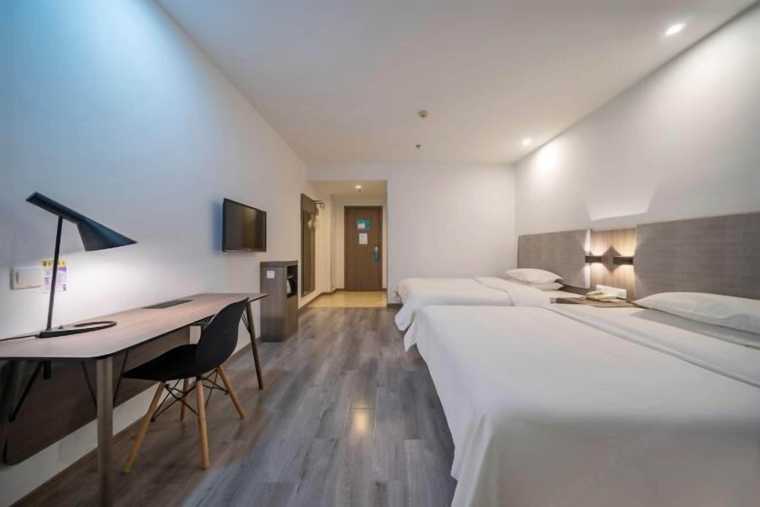 A hotel room with a desk, two beds, a TV, and a lamp.