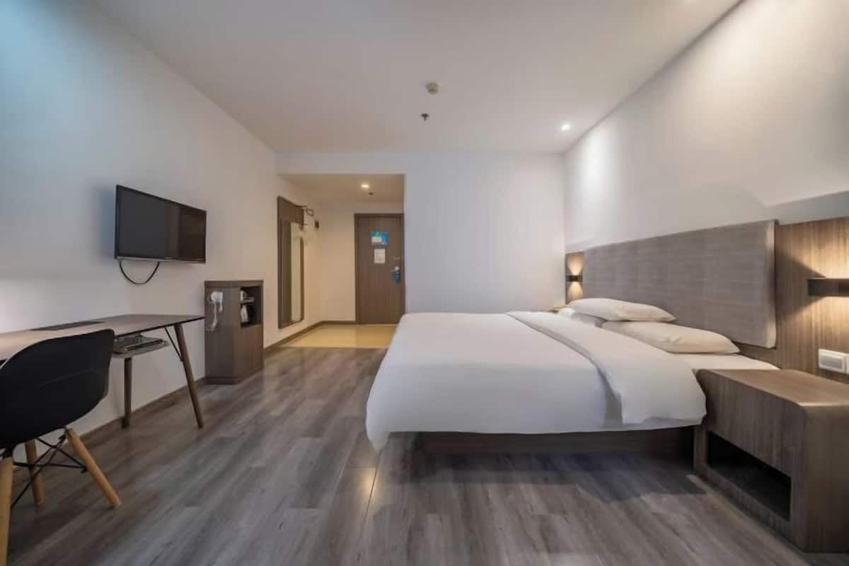 A modern hotel room with a large bed, a desk, a chair, and a television on the wall.