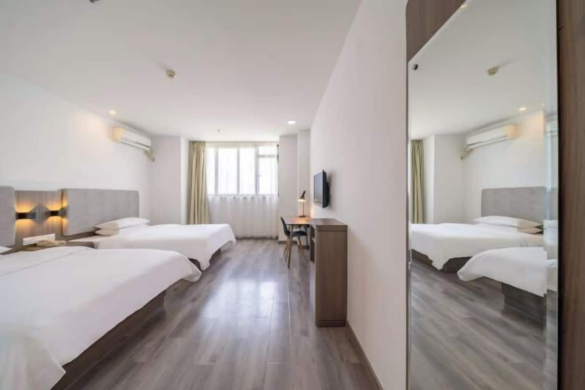 A hotel room with two beds, a desk, a chair, a TV, and a large mirror.