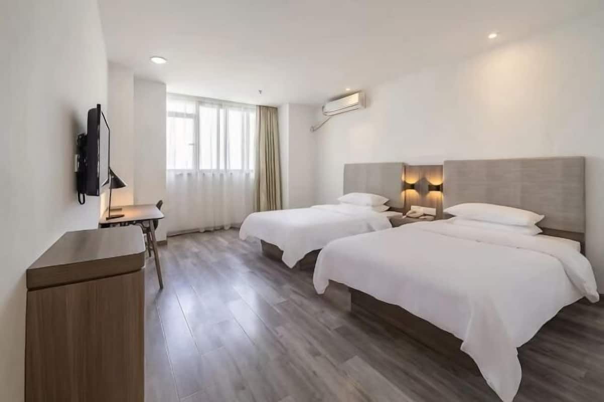 A hotel room with two beds, a desk with a lamp, a flat-screen TV, and a window with curtains.