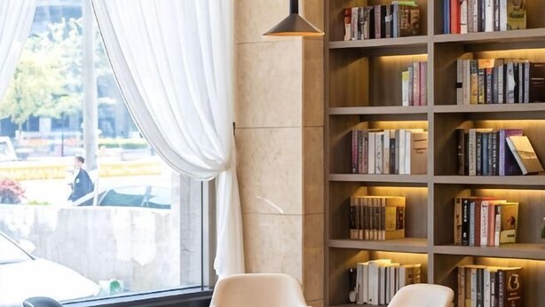 Uma biblioteca com estantes de livros, uma janela com cortinas e uma cadeira.