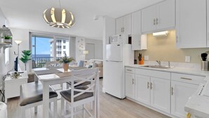 A modern kitchen with white cabinets, a built-in oven, and a large window overlooking a balcony. - GULF VIEW | 8TH FLOOR STUDIO | 2 FULL BEDS | FREE PARKING + WIFI | BEACH GEAR (Bonita Springs)