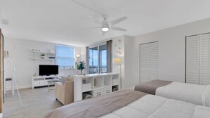 A modern hotel room with a bed, a desk with a TV, a balcony, and a ceiling fan. - GULF VIEW | 8TH FLOOR STUDIO | 2 FULL BEDS | FREE PARKING + WIFI | BEACH GEAR (Bonita Springs)