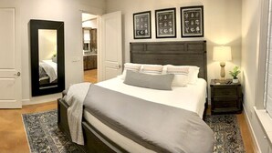 A bedroom with a bed, a nightstand, a mirror, and framed pictures on the wall.