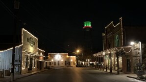 A street lined with buildings decorated with string lights, a prominent clock tower, and a clear road.