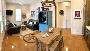 A spacious living room with a dark sofa, a coffee table, and a dining area with a wooden table and benches.