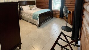 A bedroom with a bed, a ceiling fan, a window with blinds, and a fan on the floor. - Cabin On The Lake (Hemphill)