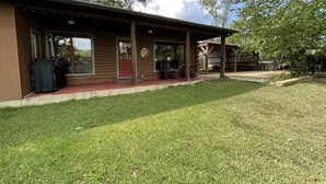 A single-story house with a covered porch, a barbecue grill, and a well-maintained lawn. - Cabin On The Lake (Hemphill)