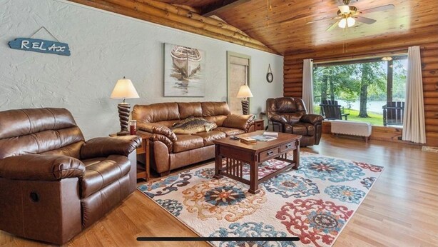 A cozy cabin interior with leather sofas, a wooden coffee table, and a large window offering a view of the outdoors. - Cabin On The Lake (Hemphill)