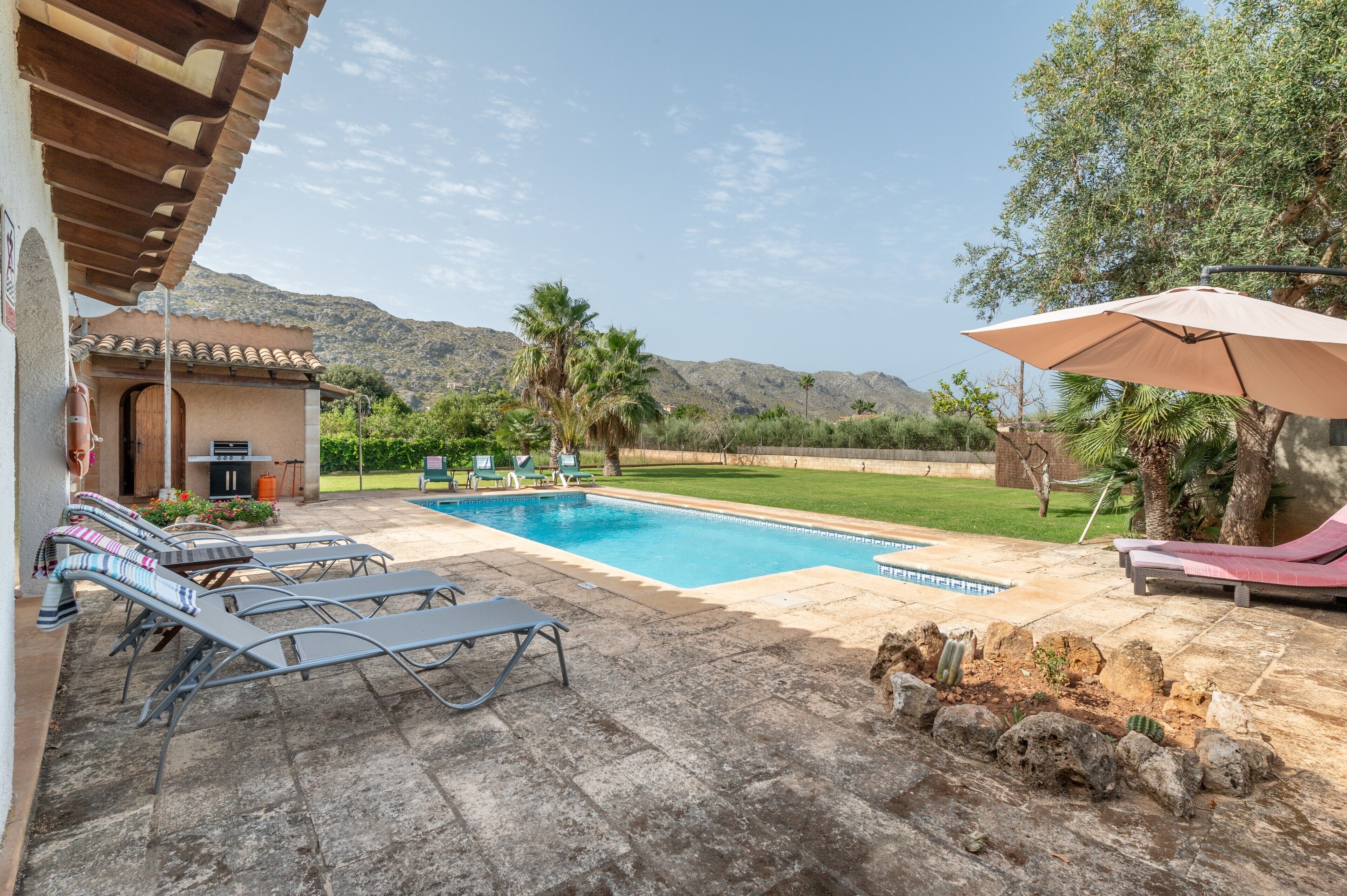 A pool area with lounge chairs, a barbecue, and a view of the mountains.