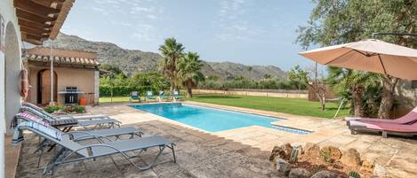 A pool area with lounge chairs, a barbecue, and a view of the mountains.